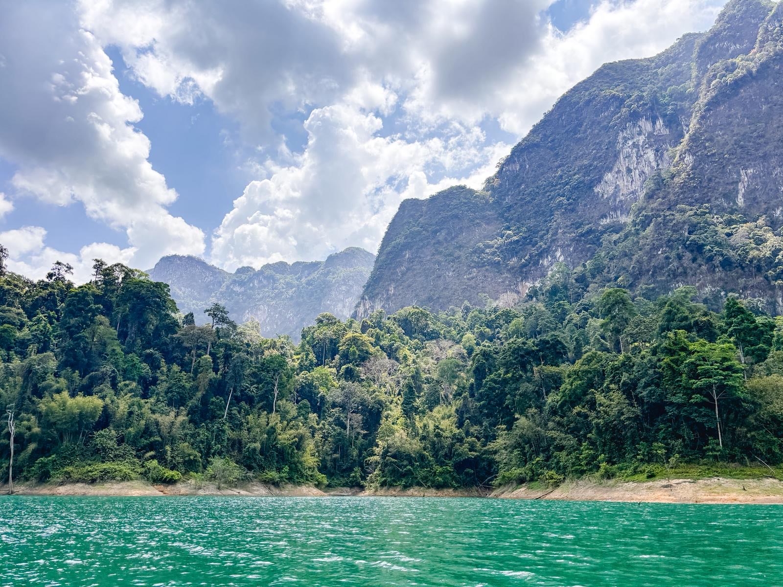 Emerald Cheow Lan Lake, jungle slopes and a karst ridge under cumulus cloud