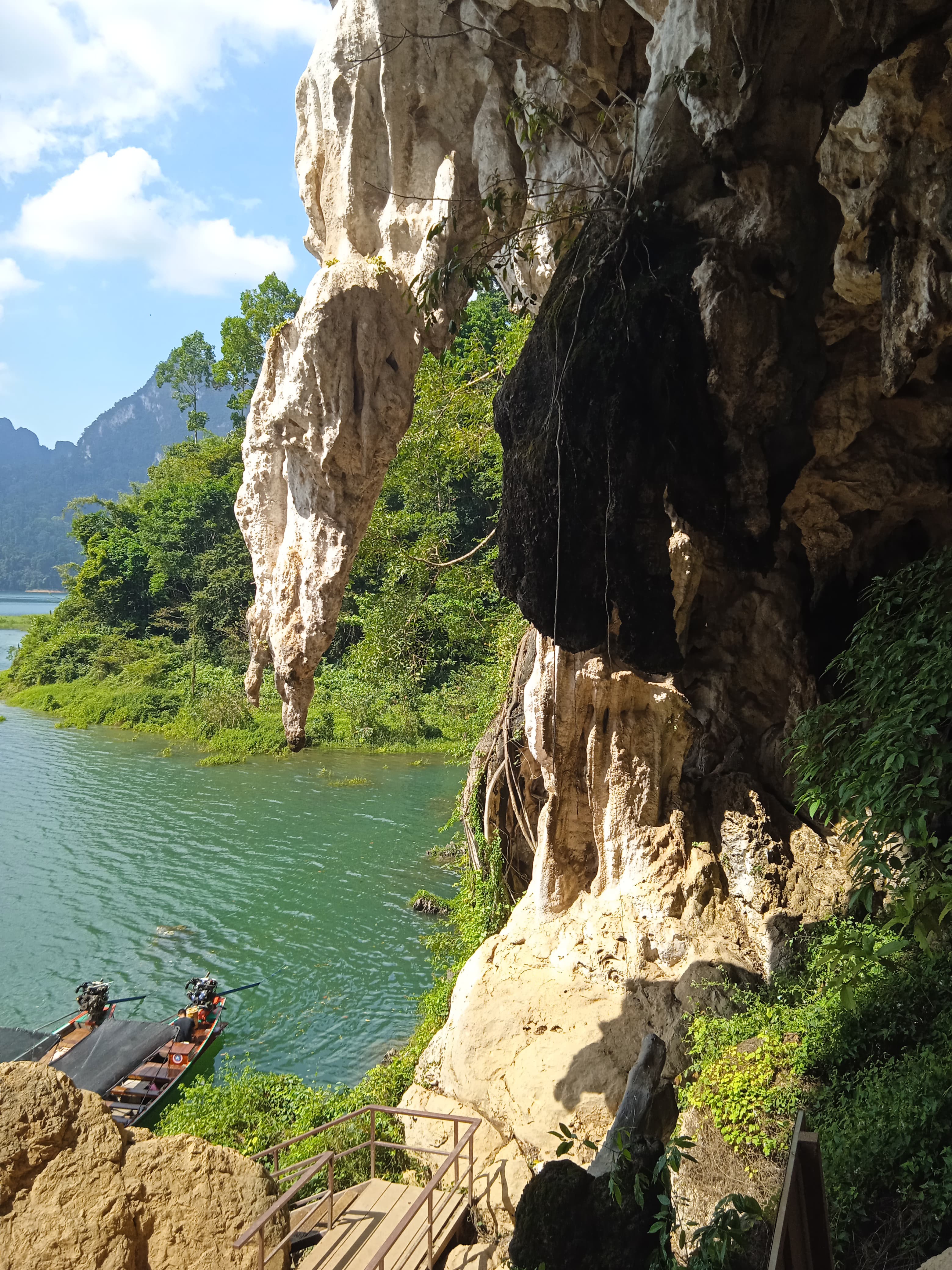 A limestone overhang with stalactites above longtail boats and a walkway