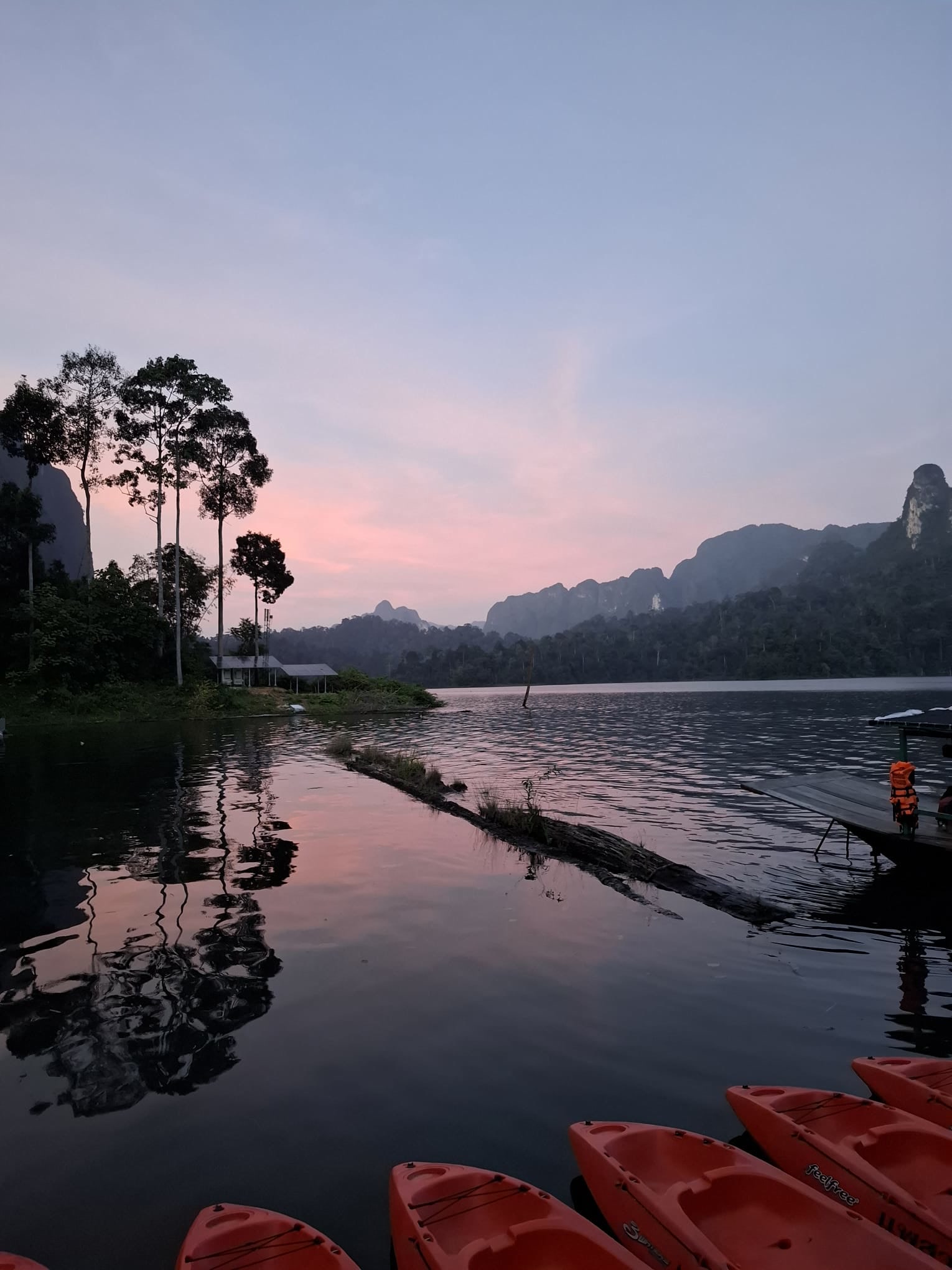 Pink dawn sky, karst reflections and red kayaks in the foreground
