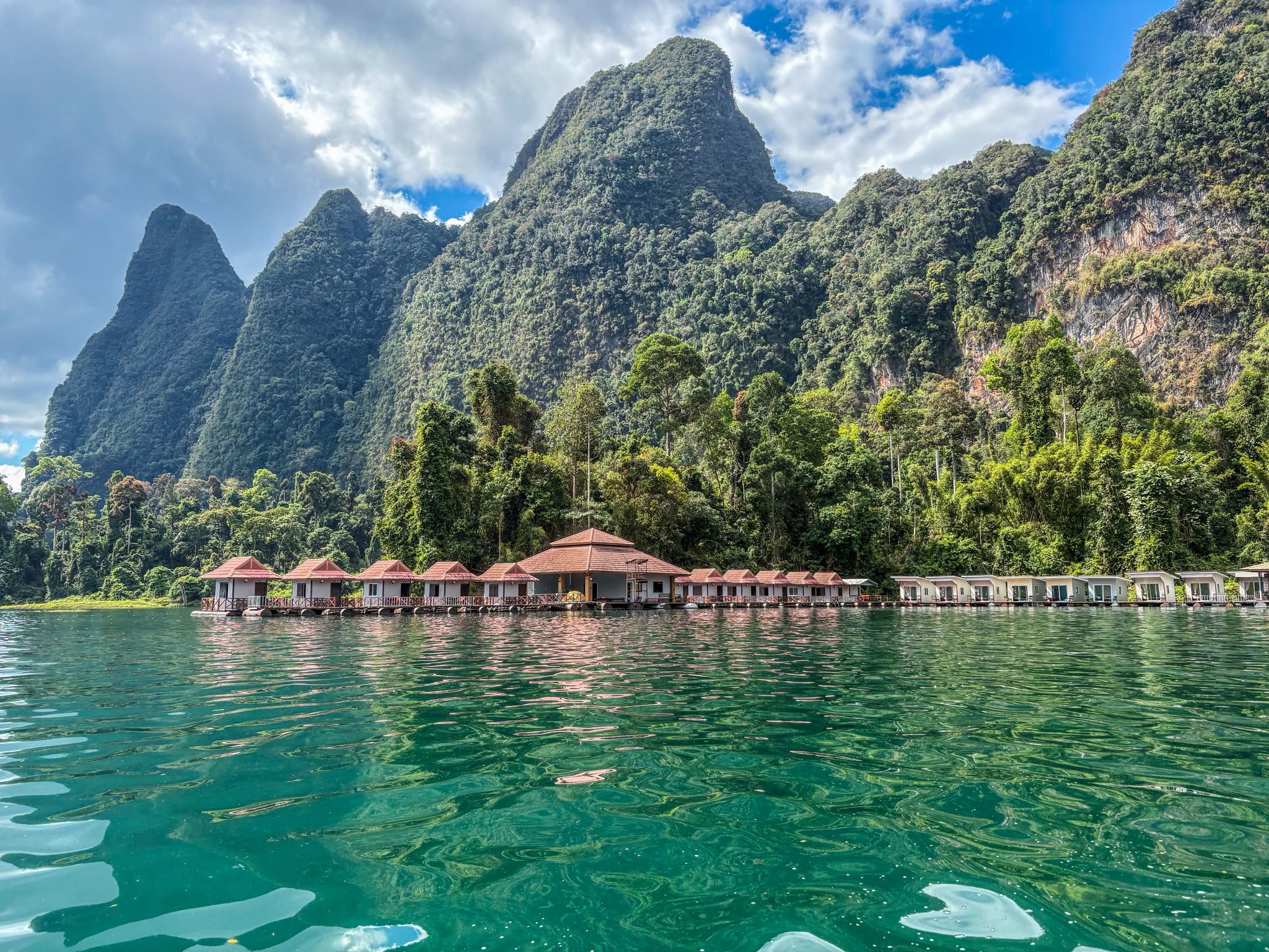 A floating raft resort with a red-roofed pavilion under towering karst peaks
