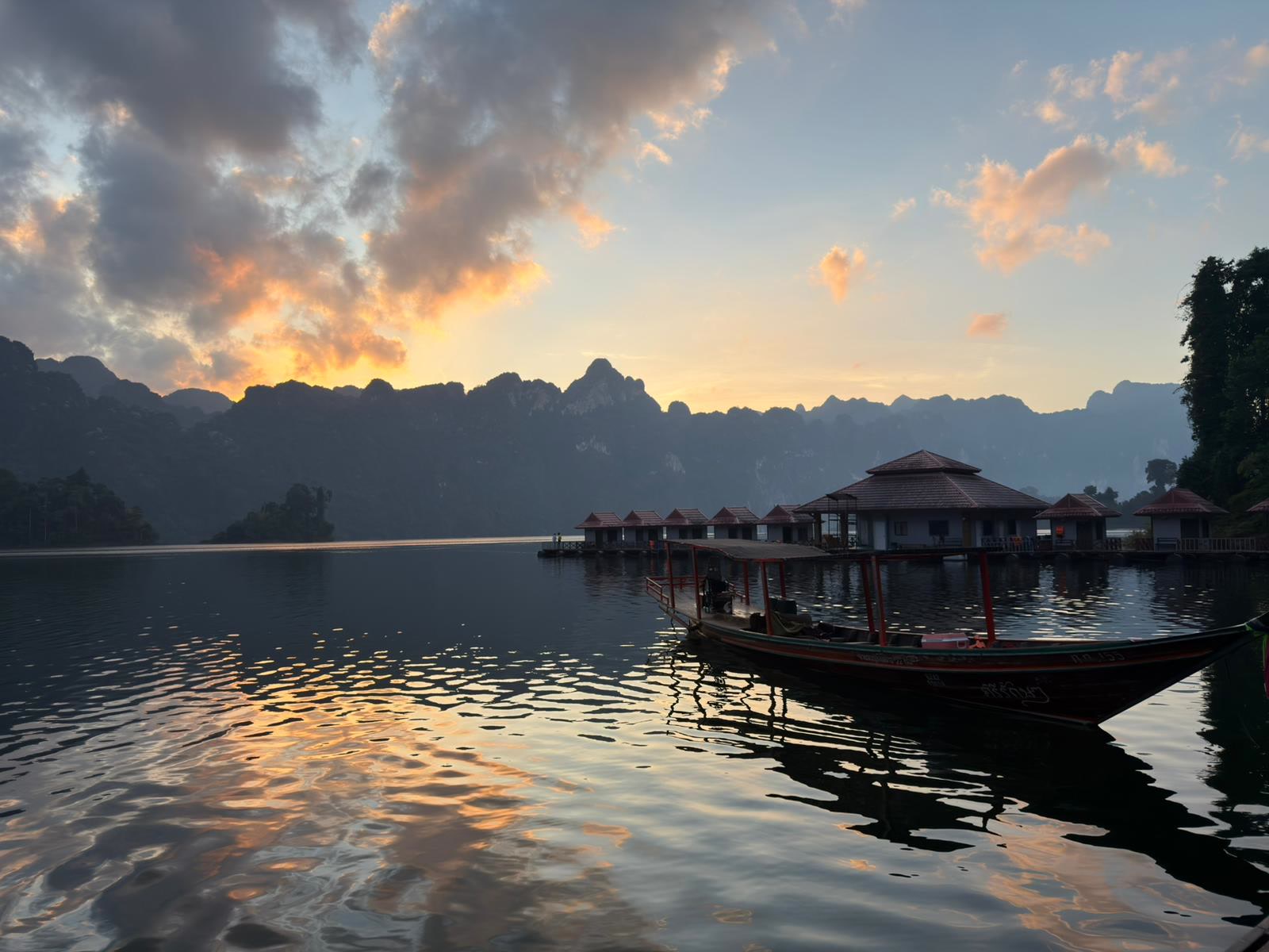 Raft houses and a longtail in silhouette on mirror-still water at sunset