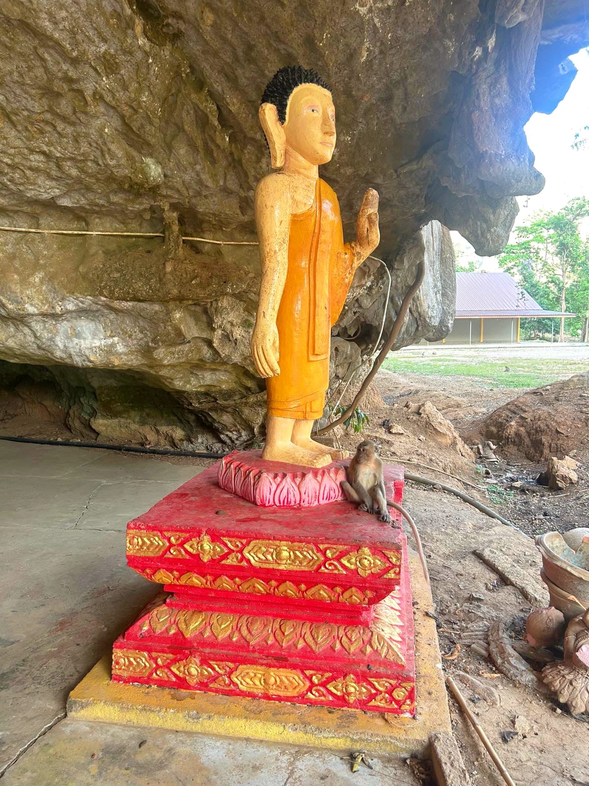 A gold standing Buddha on a red-tiered base in the cave mouth