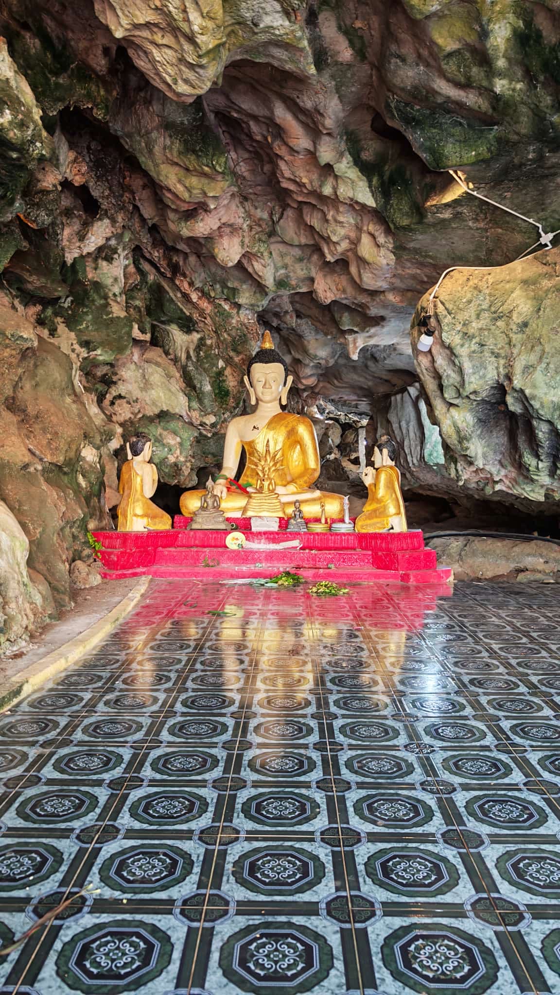 Gold Buddhas on a red platform in the cave shrine at Wat Tham Phanthurat