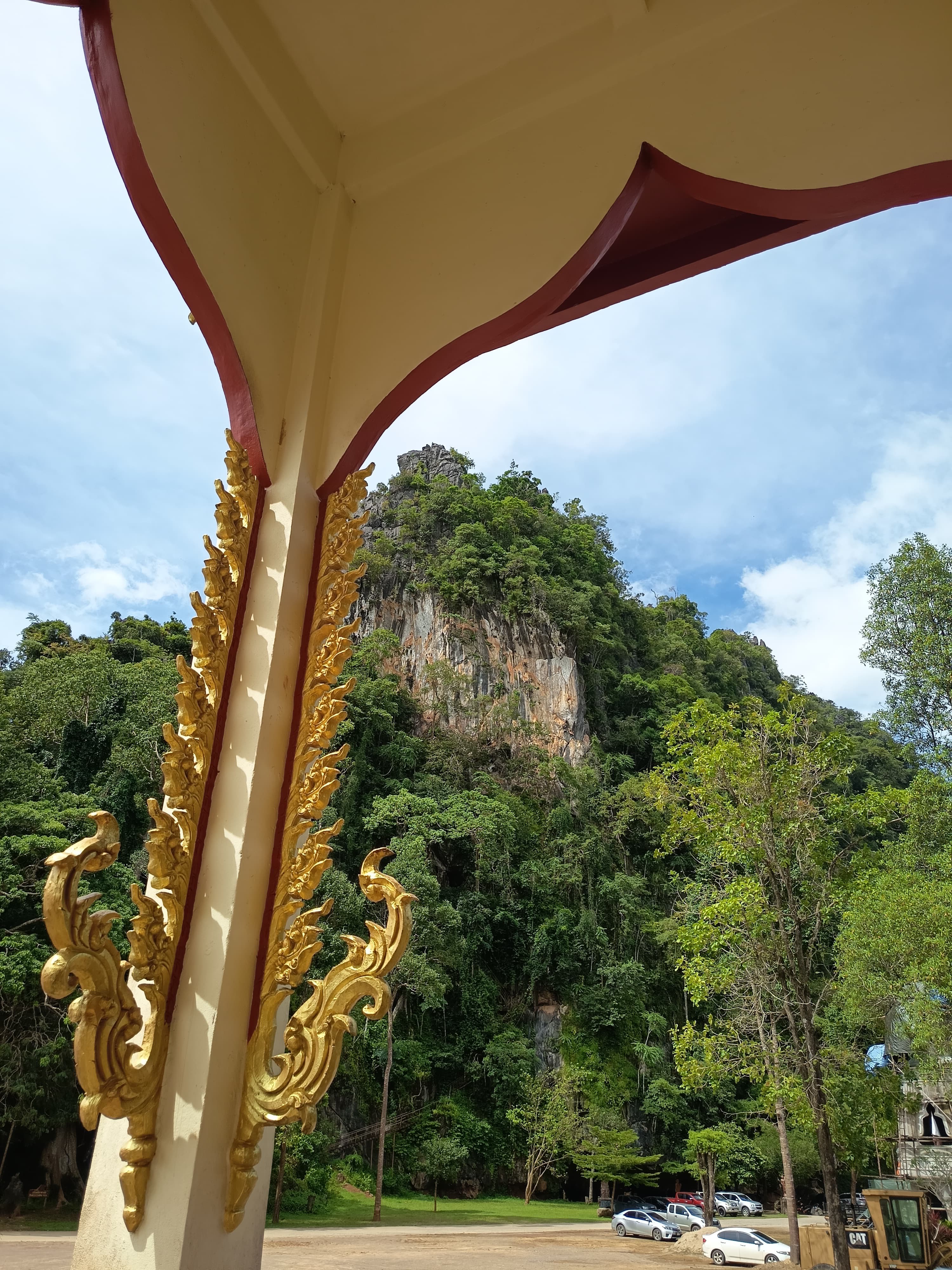 A gold naga pavilion eave framing a karst cliff at the temple